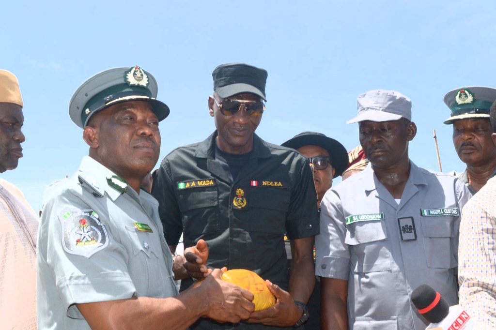 Customs Area Controller of Seme Customs Command, Nigeria Customs Service, Compt Dera Nnadi (1st from left) handing over 553 parcels of Cannabis Sativa recently seized by the command, and two (2) suspects to NDLEA officials